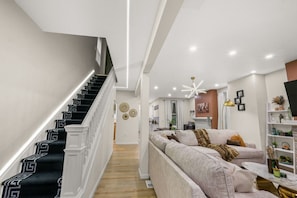 A modern interior with a staircase, a living area with a sofa, and a kitchen in the background.