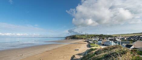 A coastal town with a sandy beach, houses, and a clear sky.