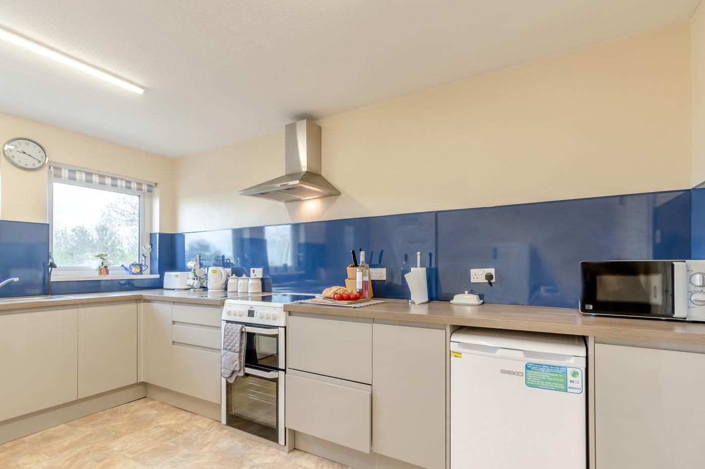 Een moderne keuken met een inbouwoven, magnetron en vaatwasser, een raam met uitzicht en een klok aan de muur.
