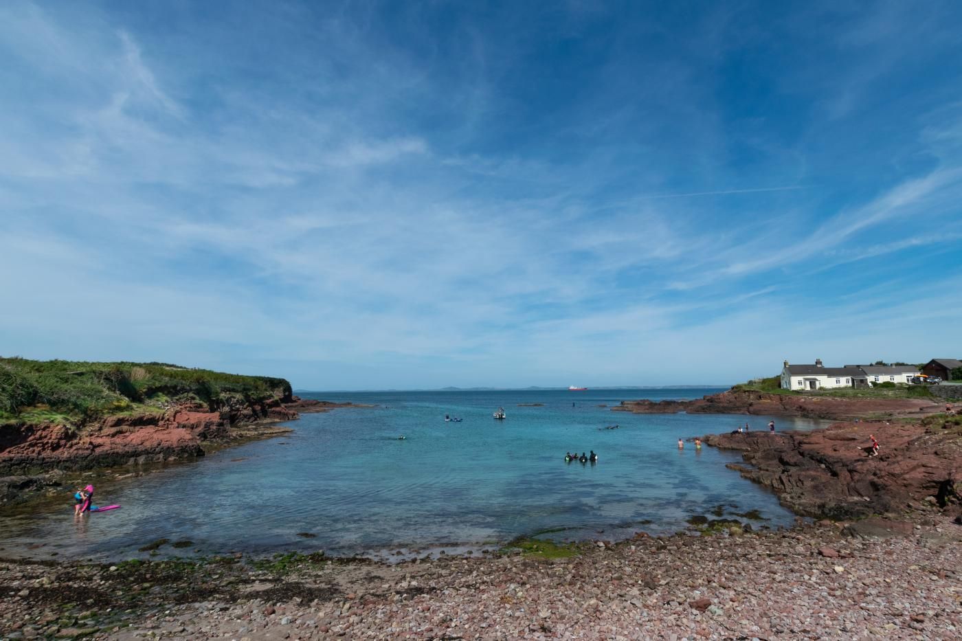 Un paysage côtier avec des rivages rocheux, une eau bleue et limpide, et quelques bâtiments sur la droite.