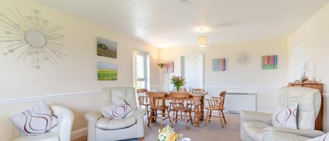 A living room with a dining area, featuring a sunburst wall decoration, a painting, and a table with chairs.