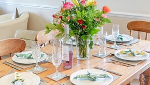 Ein Esstisch gedeckt mit Tellern, Besteck und einer Mittelanordnung aus Blumen und einer Flasche.