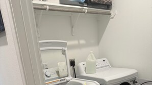 En tvättstuga med en tvättmaskin och en torktumlare som man fyller från framsidan, en flaska tvättmedel och en tvättkorg.