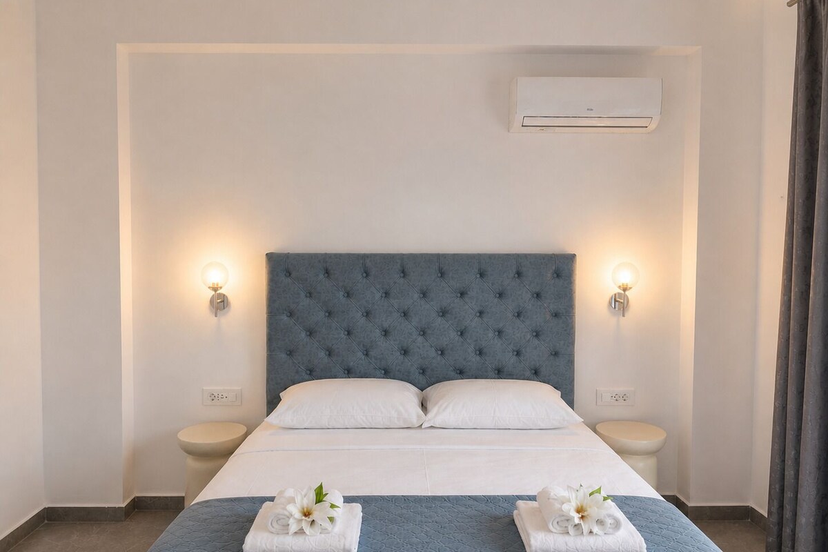 Ein Hotelzimmer mit einem großen Bett, zwei Nachttischen, einer Klimaanlage und einem Badezimmer mit Toilette und Waschbecken.