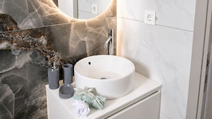 Ein Badezimmer mit Marmorwaschtisch, einem runden Spiegel und einem modernen Wasserhahn.