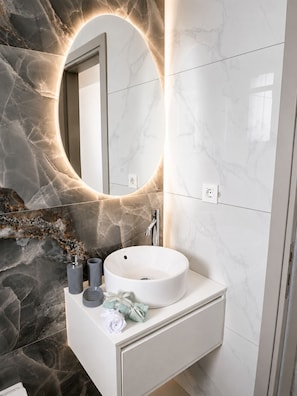 Ein Badezimmer mit Marmorwaschtisch, einem runden Spiegel und einem modernen Wasserhahn.
