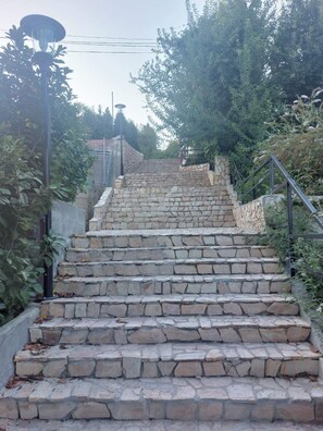A stone staircase leading up a hill, surrounded by greenery and a metal railing.