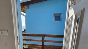 A room with a wooden floor, a door leading outside, and a view of a blue building with a balcony.
