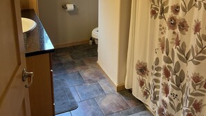 Un bagno con tenda doccia, un water, una finestra con persiane e un lavandino con un asciugamano.