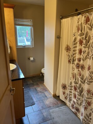 Een badkamer met douchegordijn, toilet, raam met zonwering en wastafel met handdoek.