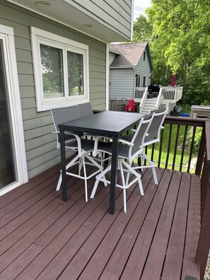 Een terras met een tafel en stoelen, een overdekt gedeelte met een bankje, en een klein huisje op de achtergrond.