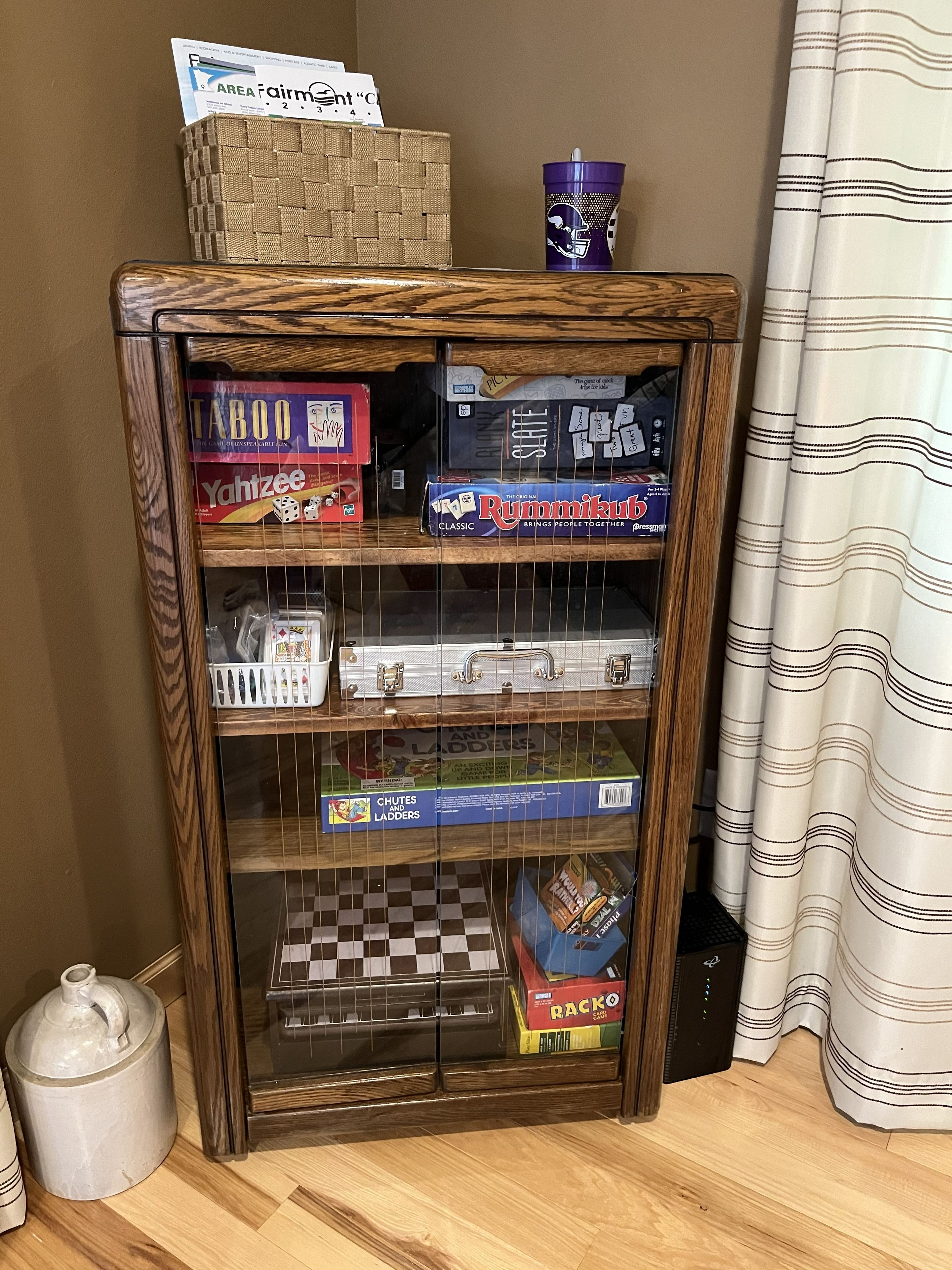 A wooden cabinet with various board games and a blue mug on top.