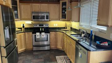 A kitchen with wooden cabinets, stainless steel appliances, a black countertop, and a window with blinds.