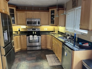 A kitchen with wooden cabinets, stainless steel appliances, a black countertop, and a window with blinds.