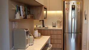 Una cocina moderna con microondas integrado, refrigerador de acero inoxidable, armarios de madera y encimera de mármol.