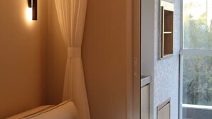 Una habitación moderna con un sofá, una lámpara de pared, una cortina translúcida y vistas por una ventana.