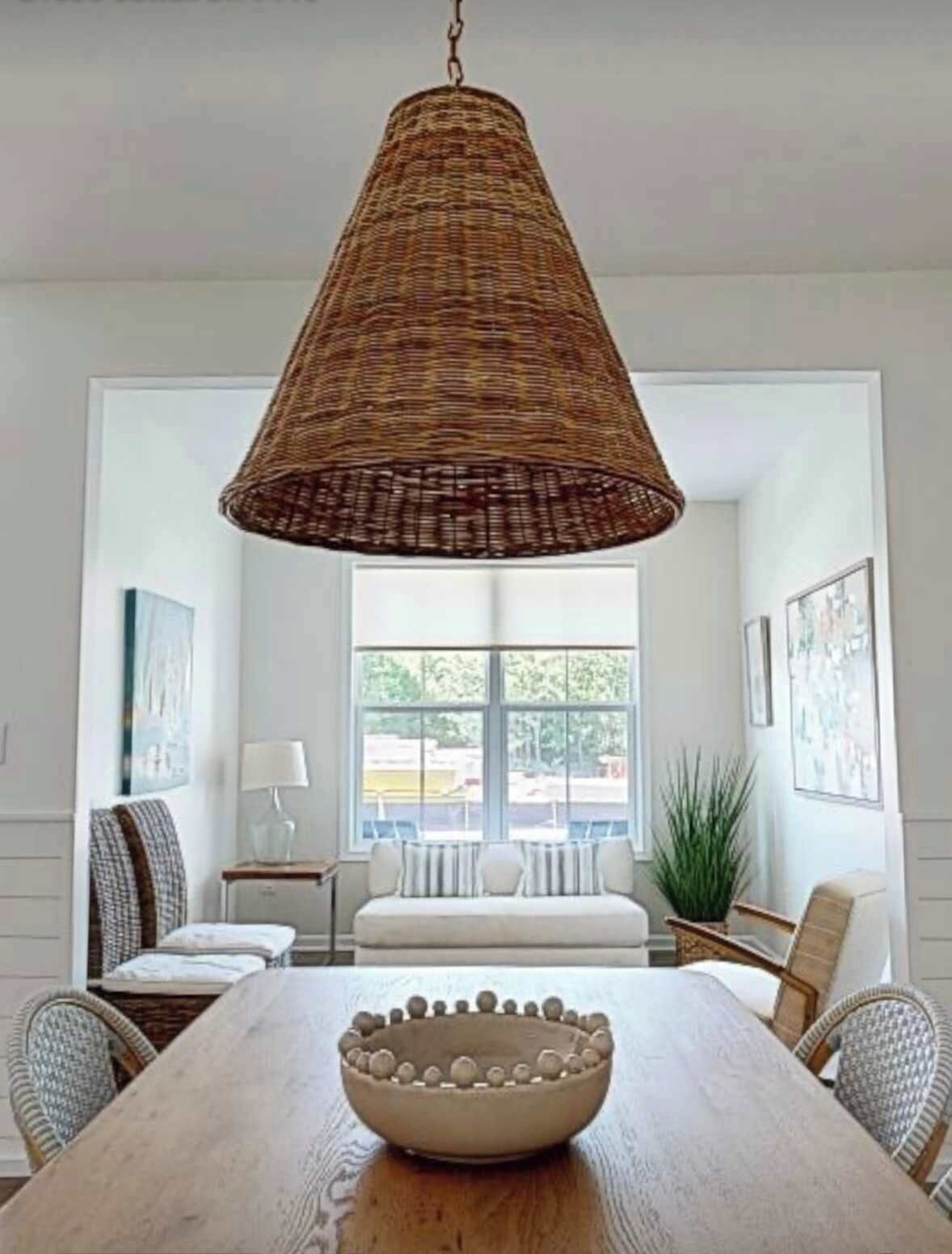 A dining area with a large wooden table, a woven pendant light, and a bowl in the center.