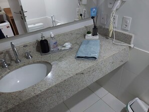 A bathroom with a granite countertop, a white sink, a mirror, a towel, a soap dispenser, and a hairdryer.