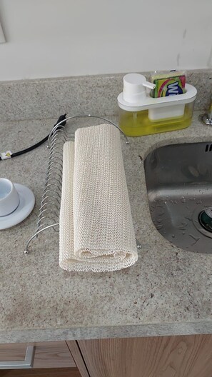 A kitchen counter with a white cloth, a dish rack, a dish soap dispenser, and a sink. - STÚDIO GRANJA BRASIL - APTO 3-414 (Petrópolis)