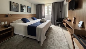 Hotellihuone, jossa on kaksi sänkyä, työpöytä, tuoli, televisio ja taideteoksia seinällä.