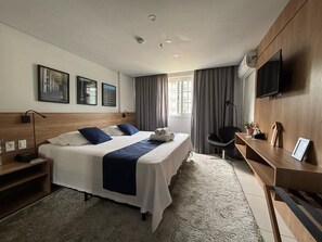A hotel room with two beds, a desk, a chair, a TV, and artwork on the wall.