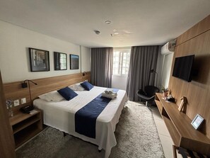 A hotel room with a large bed, a desk, a chair, a TV, and a window with curtains.