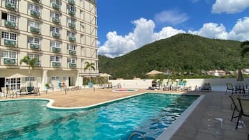 A hotel with a swimming pool, outdoor seating, and a mountain backdrop.