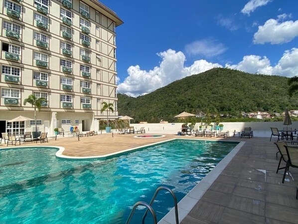 A hotel with a swimming pool, outdoor seating, and a mountain backdrop. - STÚDIO GRANJA BRASIL - APTO 3-414 (Petrópolis)