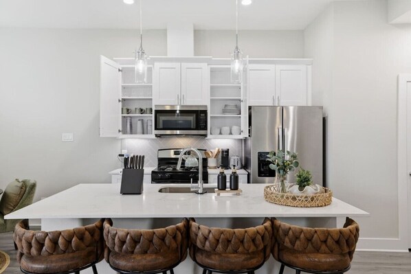 A modern kitchen with white cabinets, stainless steel appliances, and a central island with bar stools. - Gated Community | Two Homes | Sleeps 14 (Houston)