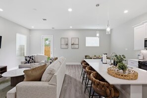 A modern kitchen with a central island, bar stools, and a dining area with a sofa. - Gated Community | Two Homes | Sleeps 14 (Houston)