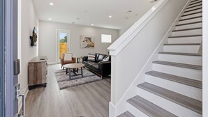 Ein modernes Interieur mit einer Treppe, einer Wohnbereits mit Sofa und Ohrensessel, sowie einem Holzschrank.