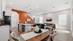 Eine moderne Küche mit Essbereich, ein Wohnzimmer mit Sofa und Fernseher sowie eine Treppe zu einer oberen Ebene.