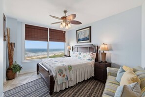 A bedroom with a bed, bedside tables, a lamp, a ceiling fan, a window with a view, and a framed picture on the wall. - Hi-Rise Condo W/ Beach Views & Resort Pool! (Galveston)