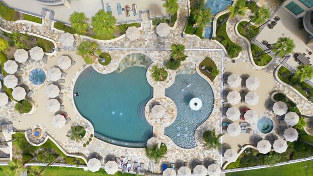 An aerial view of a resort with a central pool, surrounded by lounge areas and palm trees. - Hi-Rise Condo W/ Beach Views & Resort Pool! (Galveston)