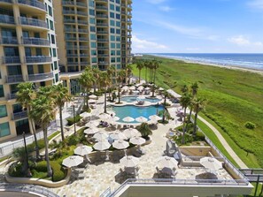 A hotel with a pool area, palm trees, and a view of the ocean. - Hi-Rise Condo W/ Beach Views & Resort Pool! (Galveston)