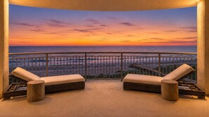 A balcony with two cushioned chairs and a small round table, overlooking a sunset view. - Hi-Rise Condo W/ Beach Views & Resort Pool! (Galveston)