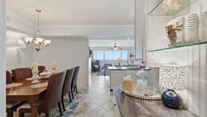 A dining area with a chandelier, a kitchen with a glass display case, and a view to the living area. - Hi-Rise Condo W/ Beach Views & Resort Pool! (Galveston)