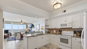 A spacious kitchen with white cabinetry, a central island, and a view to a balcony. - Hi-Rise Condo W/ Beach Views & Resort Pool! (Galveston)