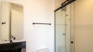 Ein Badezimmer mit Duschkabine aus Glas, Waschbecken in Schwarz, einem Spiegel und einem Handtrockner.