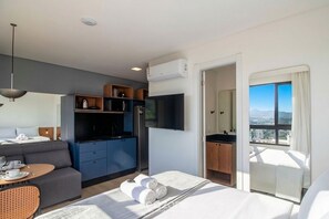 Ein modernes Hotelzimmer mit Bett, Essbereich, Küchenzeile und Balkon mit Blick auf die Stadt.