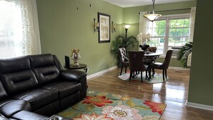 A living room with a leather sofa, a dining area with a table and chairs, a floral rug, and a green wall. - Bright and Airy 3 BRM - 1 BATH -5 Mins to Falls (Niagara Falls)
