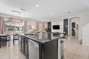 A modern kitchen with a central island, dining area with chairs, and a flat-screen TV mounted on the wall. - 8BR Disney-Area Resort Home, Private Pool, Game Room | Sleeps 17,Lazy River-7054 (Davenport)