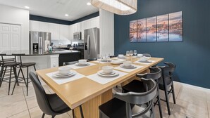 A modern kitchen with white cabinets, stainless steel appliances, and a dining area with a long table set for six. - 8BR Disney-Area Resort Home, Private Pool, Game Room | Sleeps 17,Lazy River-7054 (Davenport)