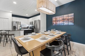 A modern kitchen with white cabinets, stainless steel appliances, and a dining area with a long table set for six. - 8BR Disney-Area Resort Home, Private Pool, Game Room | Sleeps 17,Lazy River-7054 (Davenport)