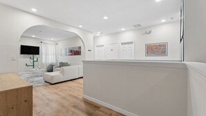 A modern living room with a white sofa, a wooden coffee table, and a flat-screen TV mounted on the wall. - 8BR Disney-Area Resort Home, Private Pool, Game Room | Sleeps 17,Lazy River-7054 (Davenport)