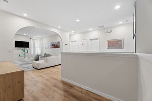 A modern living room with a white sofa, a wooden coffee table, and a flat-screen TV mounted on the wall. - 8BR Disney-Area Resort Home, Private Pool, Game Room | Sleeps 17,Lazy River-7054 (Davenport)