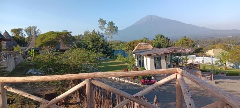 Un puente de madera que lleva a una peque ña construcción con techo de paja, rodeada de vegetación y una montaña al fondo.