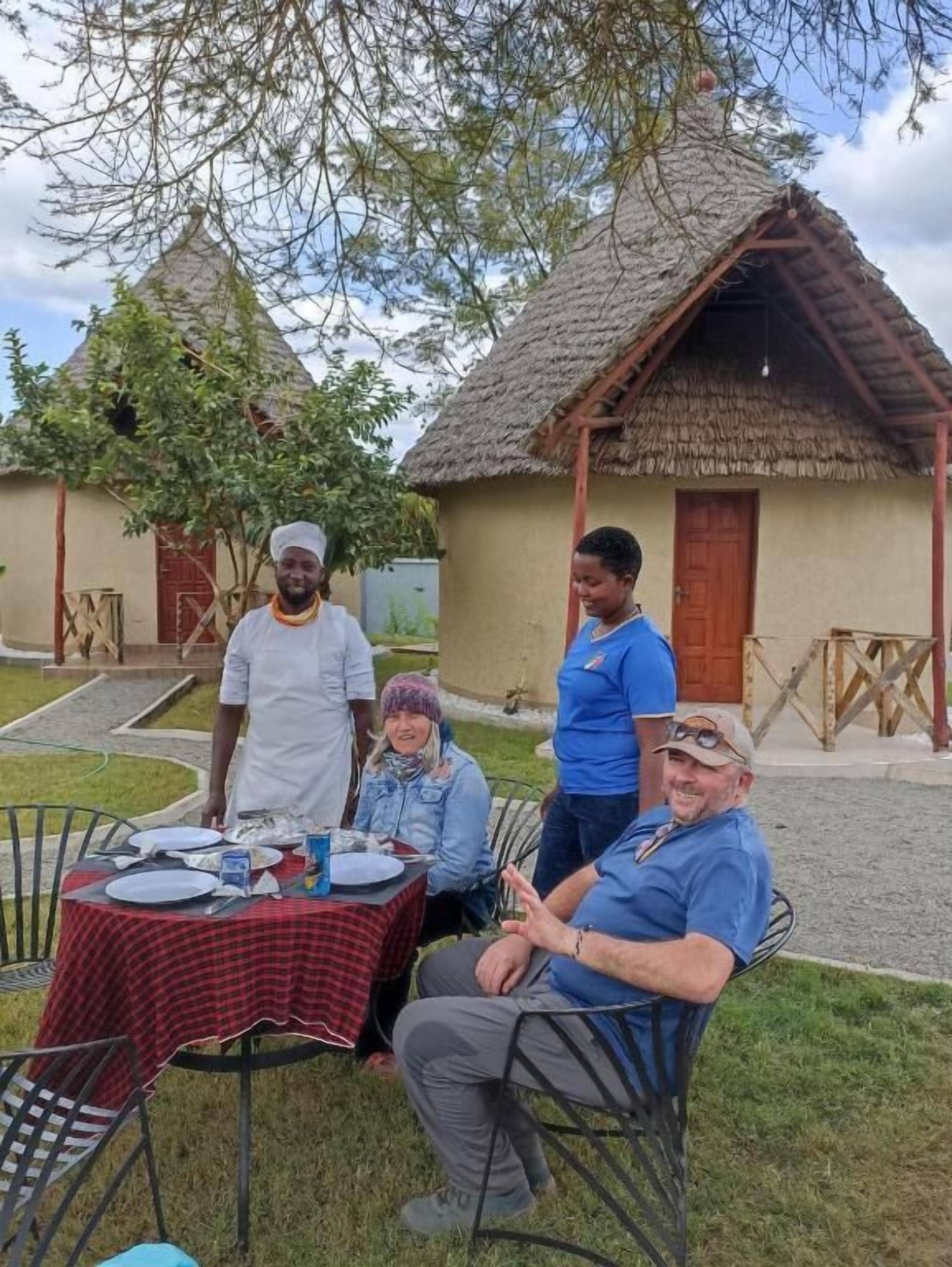 Un grupo de personas sentadas en una mesa al aire libre con mantel a cuadros, rodeadas de sillas.