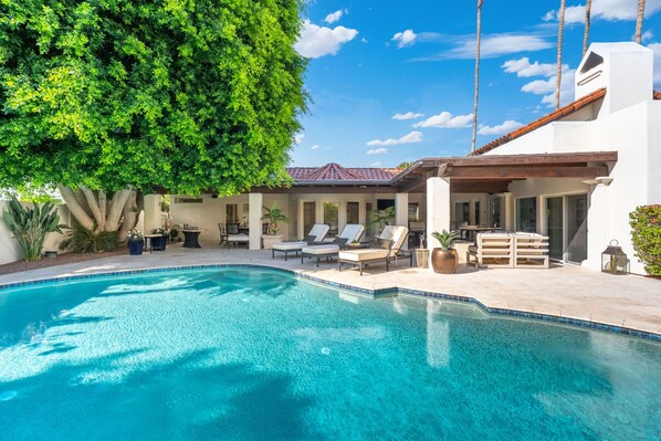 Ein Schwimmbecken mit Liegestühlen, einer Pergola und einem weißen Gebäude mit Ziegeldach.