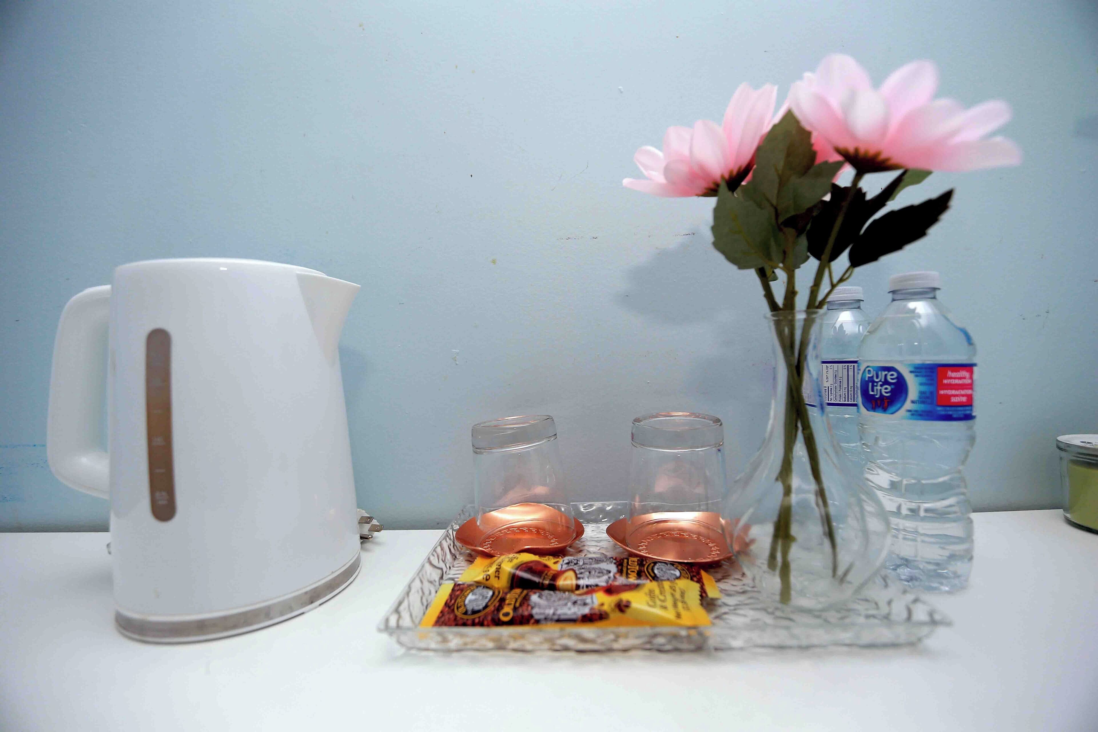 Een wit waterkoker, twee glazen, een vaas met roze bloemen en twee waterflessen op een dienblad.